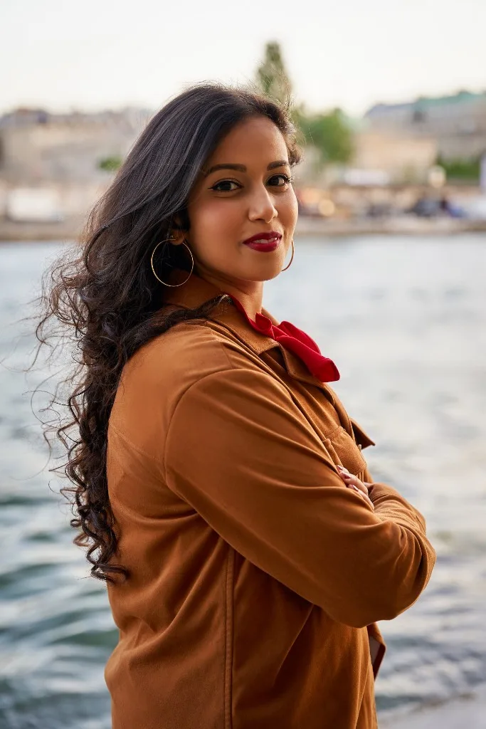 Sara Abu by the water, in a brown jacket and a red scarf.